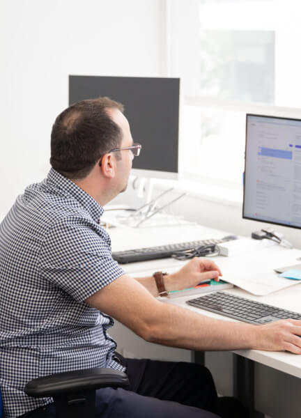 A man sitting at a desk, using a computer with a monitor beside him